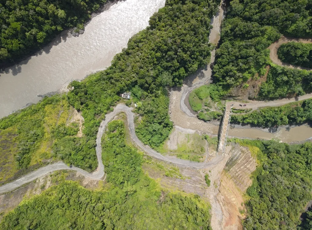 Aerial view of a winding road cut through forested hills beside a river