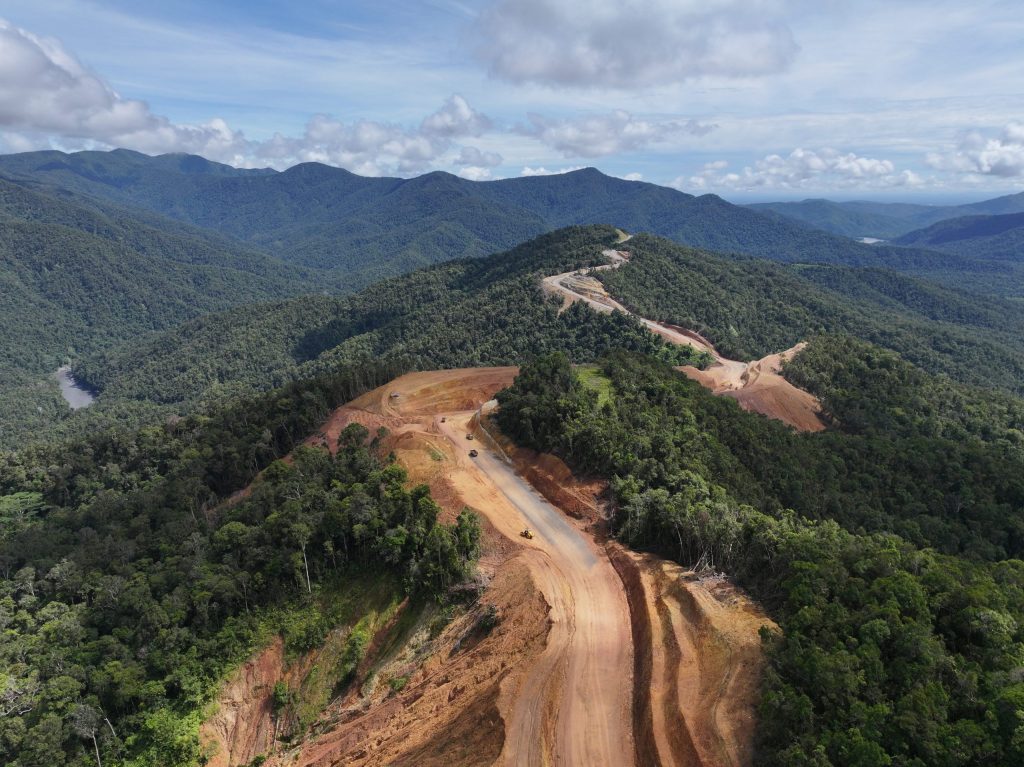 Aerial view of an unpaved road being cut along forested mountain ridges