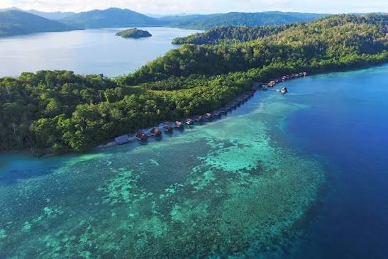 Aerial view of stilt houses along a forested coast above a coral reef
