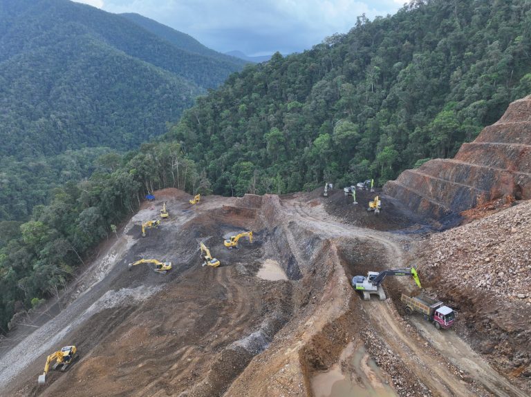 Excavators cutting a road into a steep forested mountainside