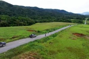 A two-lane road running through grassland below forested hills