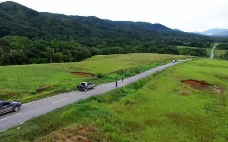 A two-lane road running through grassland below forested hills