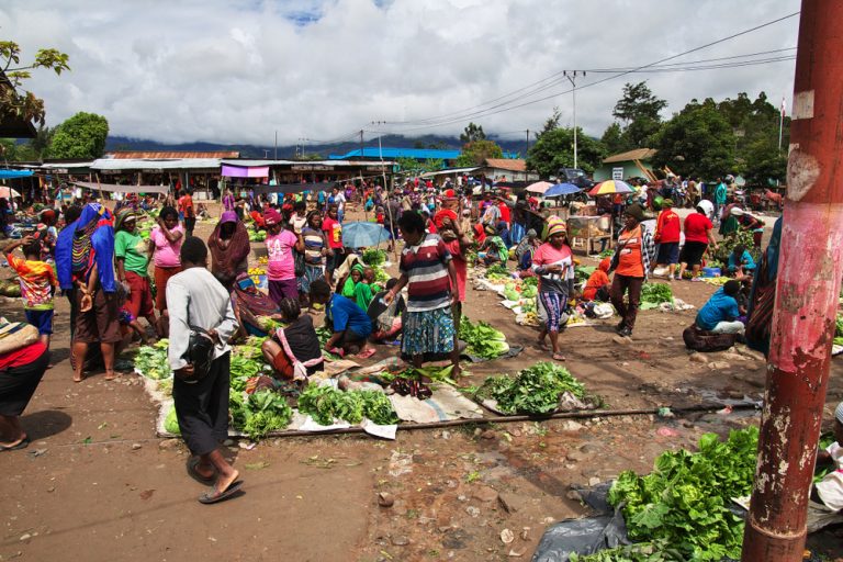 Busy morning market with vendors selling vegetables on the ground.