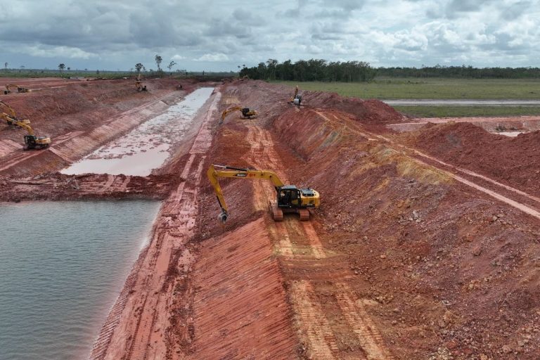 Excavators digging a wide drainage canal on flat cleared land