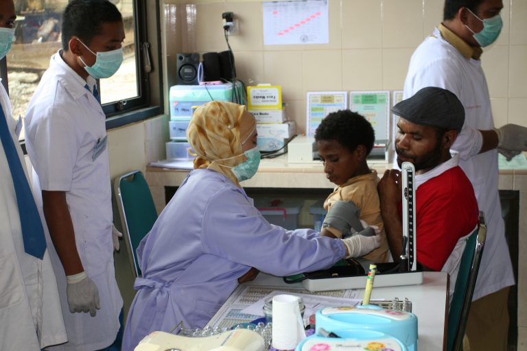 A health worker examining a boy at a clinic while a man holds him