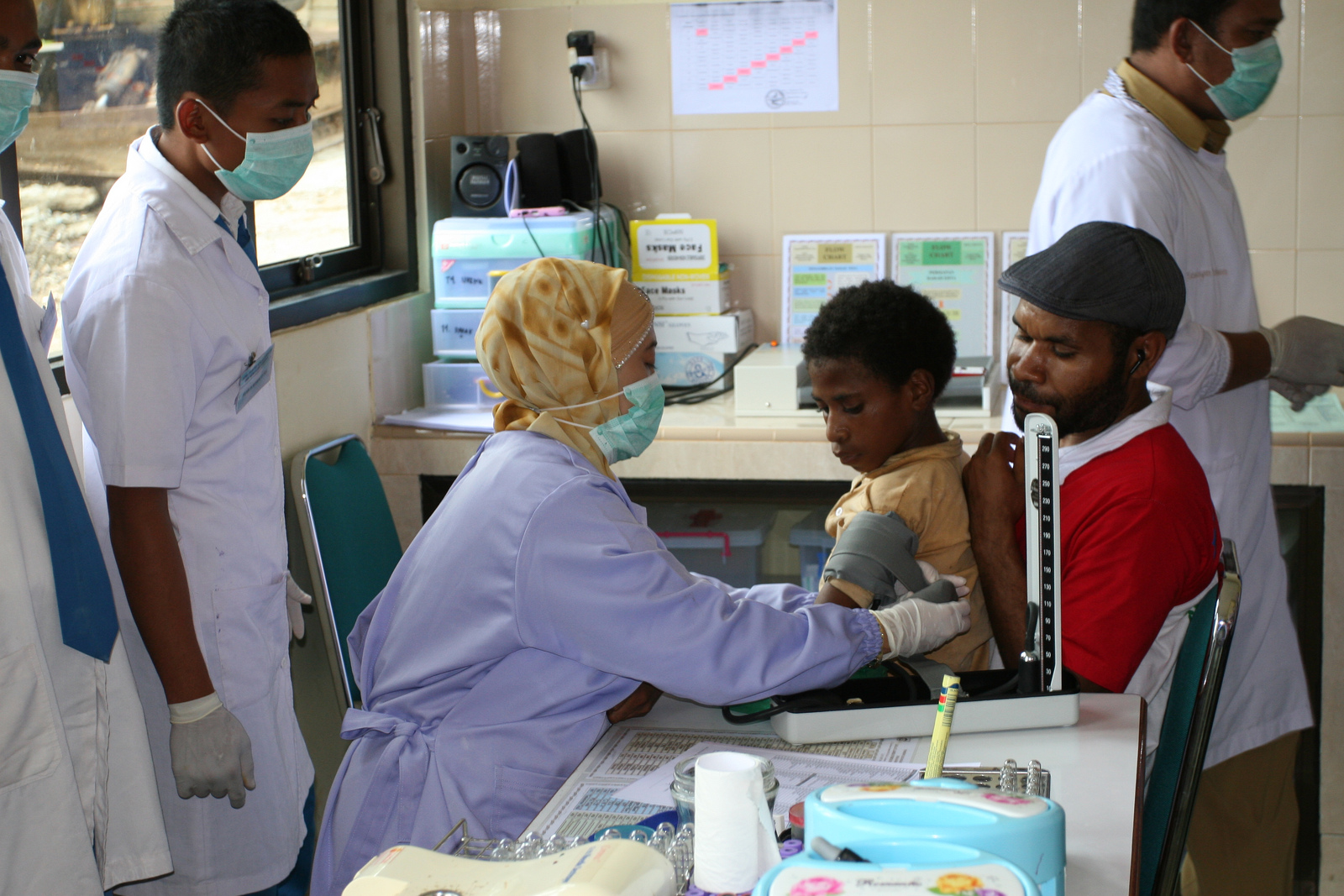 A health worker examining a boy at a clinic while a man holds him