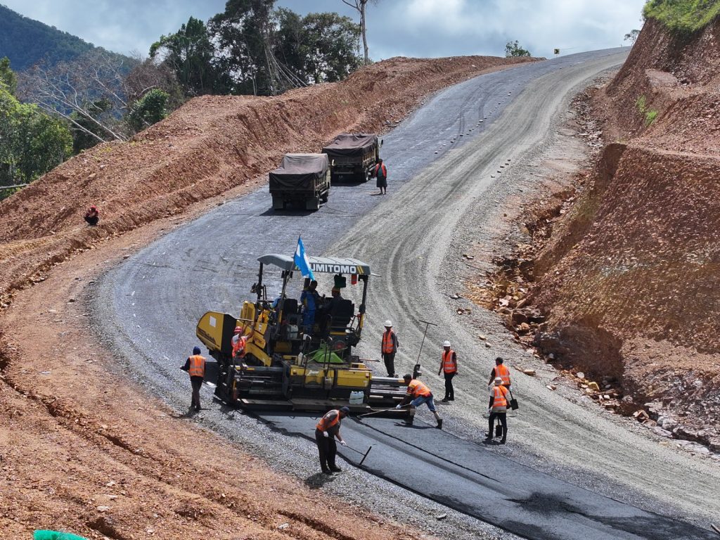 Road workers laying asphalt on a newly cut hillside road