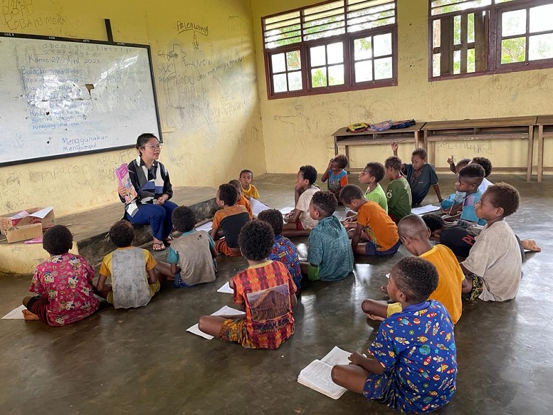Children sitting on a classroom floor reading with a teacher