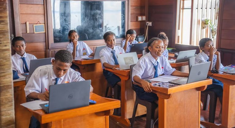 Secondary school students in uniform working on laptops in a classroom.