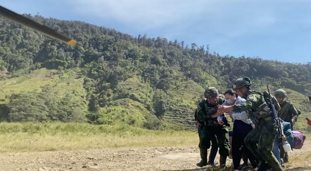 Soldiers helping a woman across an airstrip in a highland valley