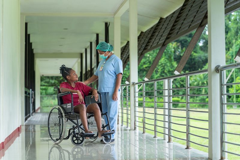 Nurse assisting a patient in a wheelchair along a hospital corridor.