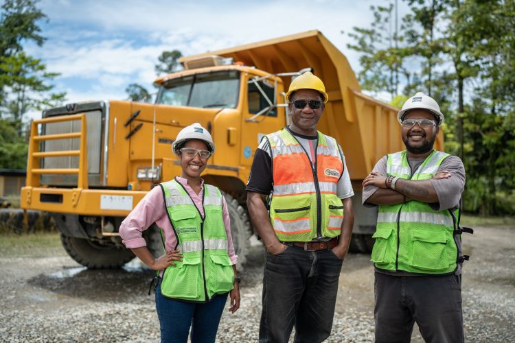 Three workers in safety vests and helmets in front of a large dump truck