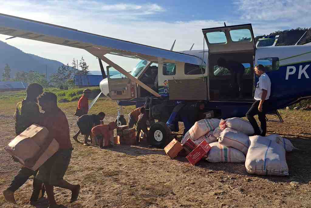 People unloading sacks of goods from a small aircraft at a rural airstrip.