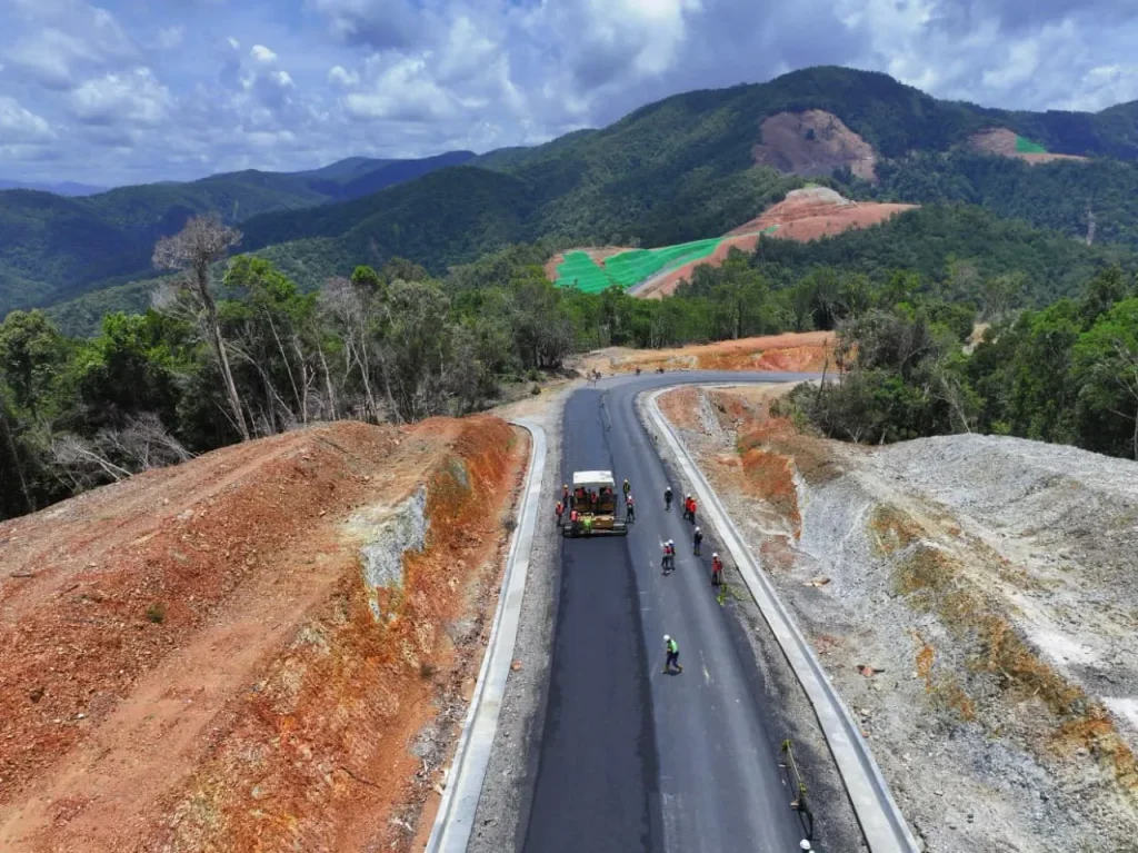Newly paved road winding through hills, with road workers.