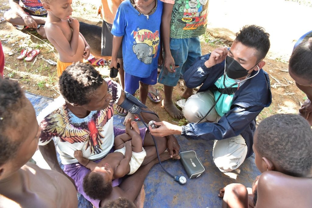 Health worker checking a child with a stethoscope as villagers watch.