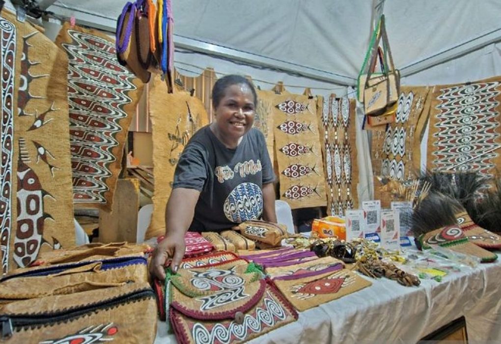 Woman selling handmade bags and crafts at an exhibition stall.