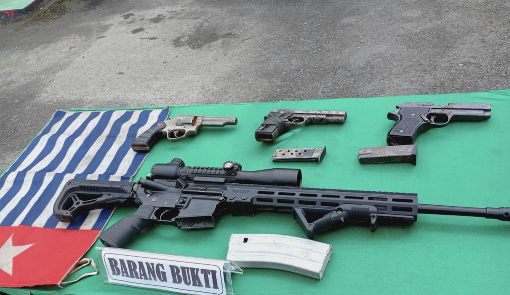 Surrendered combat gear, including a precision rifle fitted with an optical scope, sidearms, and insignia, displayed during disarmament proceedings in Mulia, Puncak Jaya.