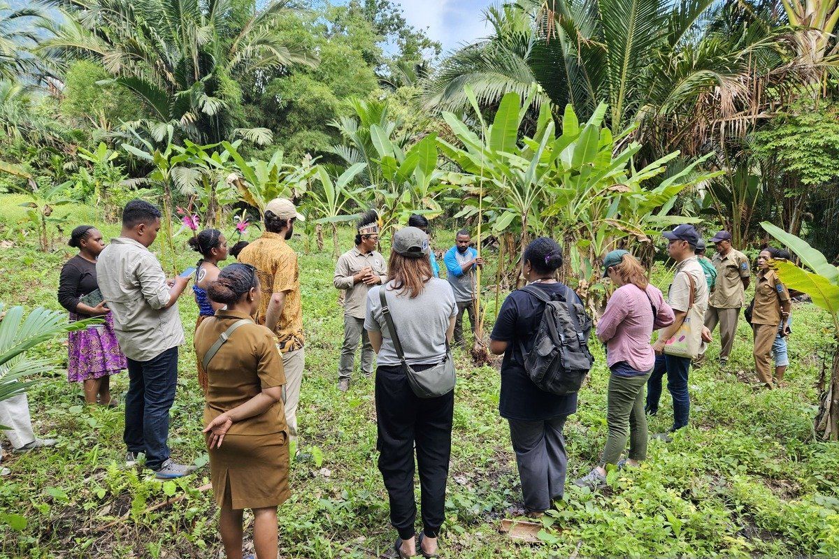 Residents and officials standing together in a village garden among banana plants.