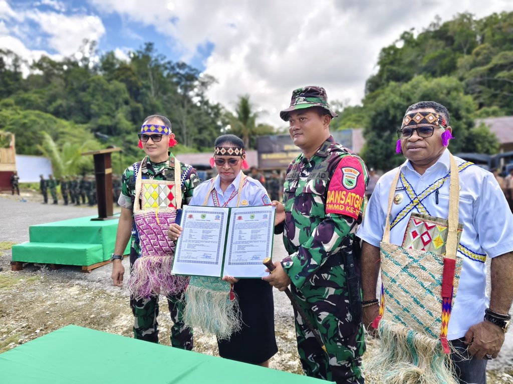 Officials and a soldier holding a signed agreement at an outdoor ceremony.