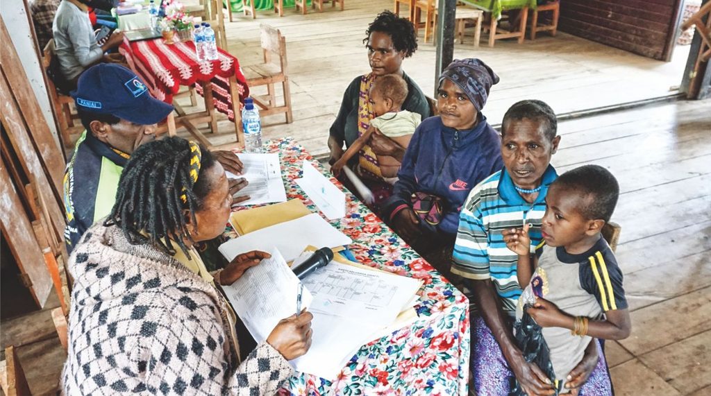 Mothers and children registering at a village public service desk.