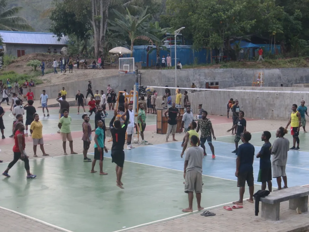 Young people playing volleyball and football on an outdoor community court.