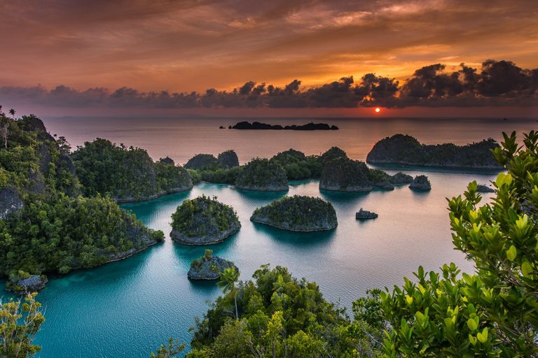 Sunset over small forested limestone islands in a lagoon.