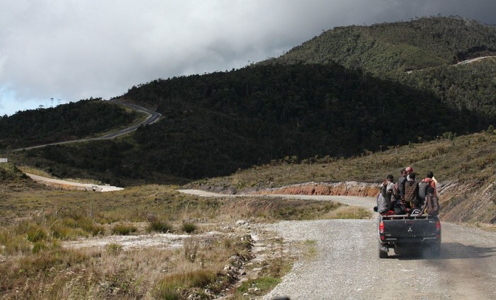 Pickup truck carrying passengers on an unpaved mountain road.