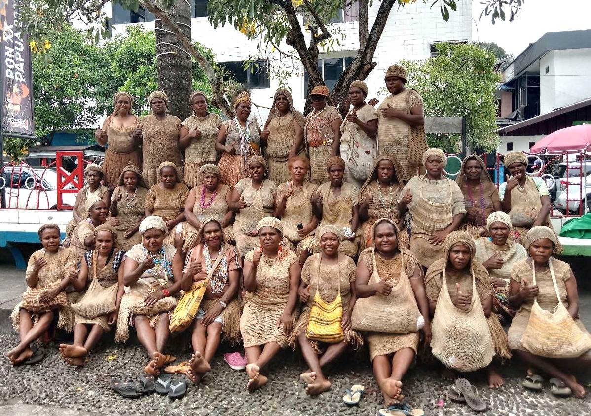 Group of Papuan women in matching traditional dress with noken bags.