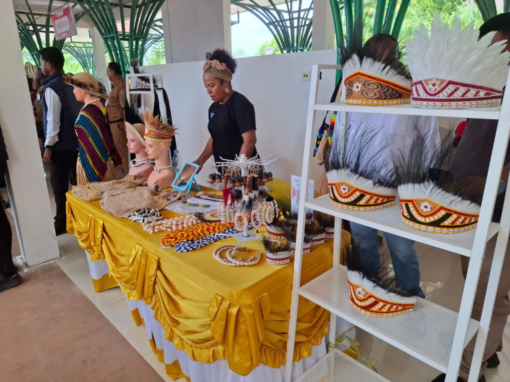 Woman arranging traditional feather headdresses and crafts at an exhibition stand.