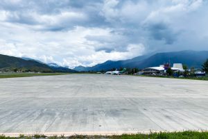 Wide concrete apron of Wamena Airport with a passenger plane and terminal below green mountains