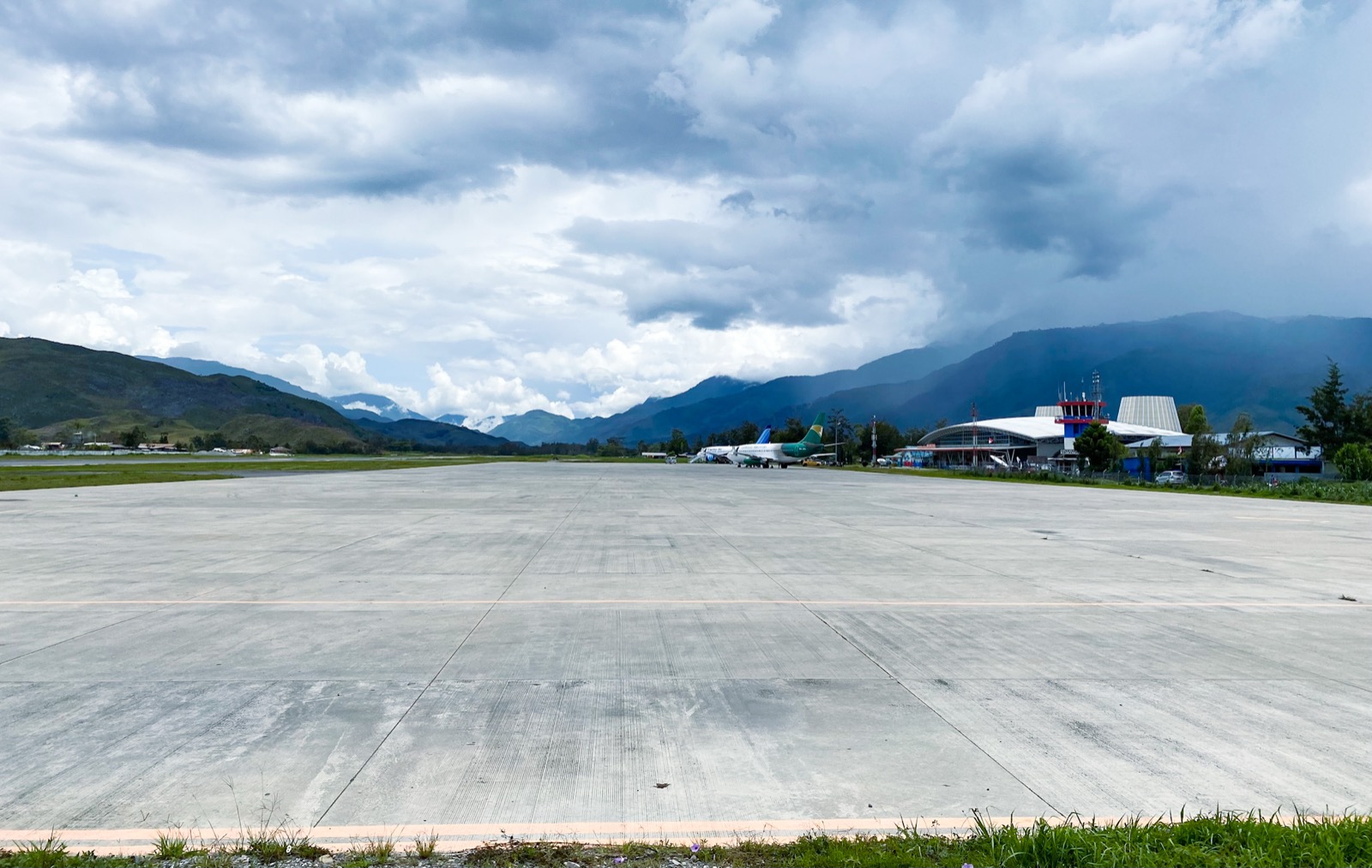 Wide concrete apron of Wamena Airport with a passenger plane and terminal below green mountains
