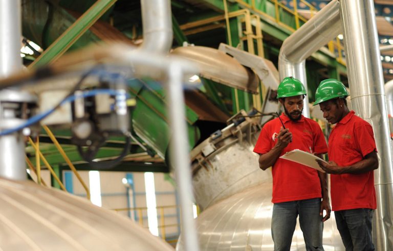 Two workers in hard hats checking a clipboard inside a processing plant.