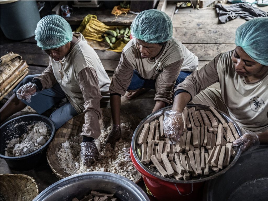 Women in hairnets preparing traditional food in a kitchen.