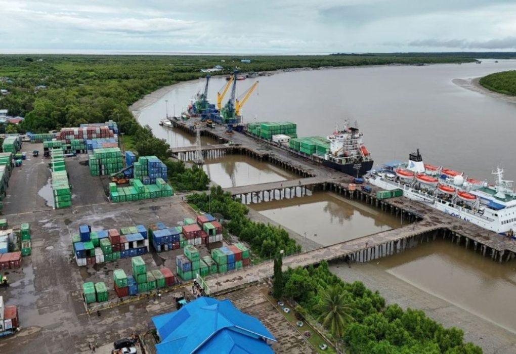 Aerial view of a river port with stacked containers and a passenger ship.
