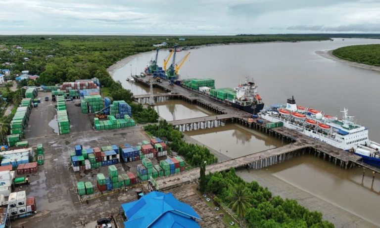 Aerial view of a river port with stacked containers and a passenger ship.
