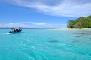 Speedboat crossing turquoise water near a white-sand island beach in Papua.