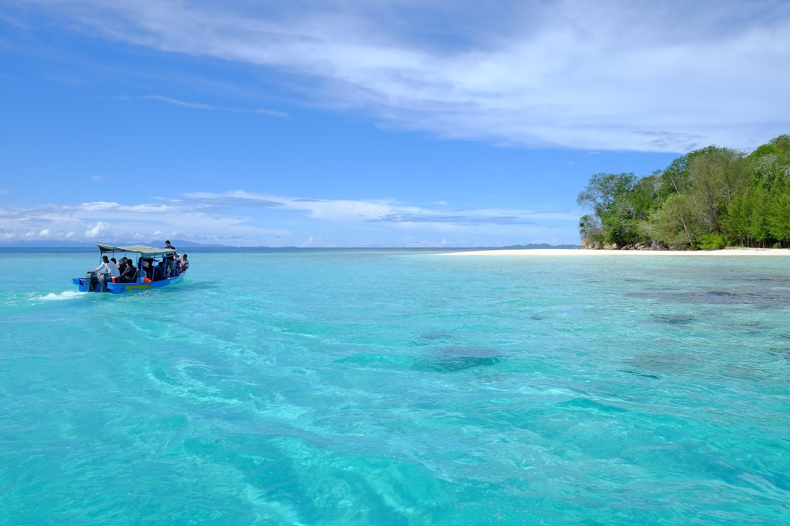 Speedboat crossing turquoise water near a white-sand island beach in Papua.