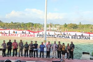 Officials stand in front of a long banner reading Selamat Datang Provinsi Papua Selatan at a public celebration in Merauke