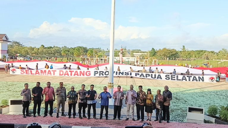 Officials stand in front of a long banner reading Selamat Datang Provinsi Papua Selatan at a public celebration in Merauke