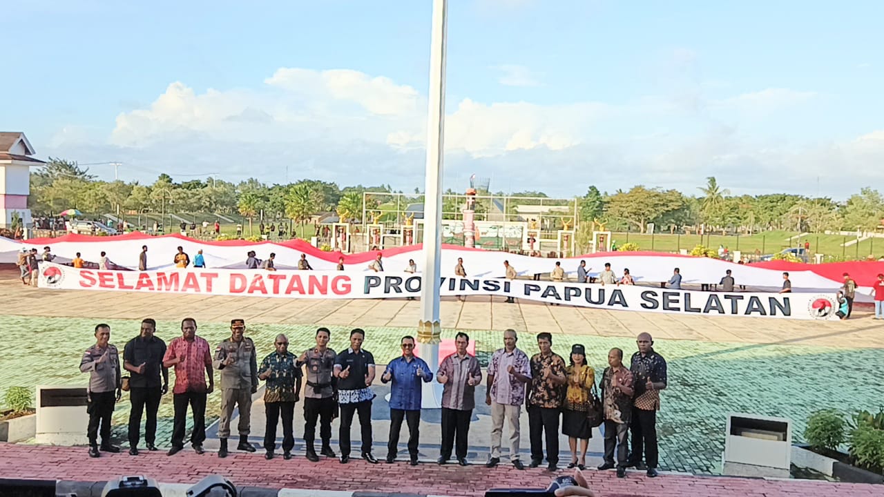 Officials stand in front of a long banner reading Selamat Datang Provinsi Papua Selatan at a public celebration in Merauke
