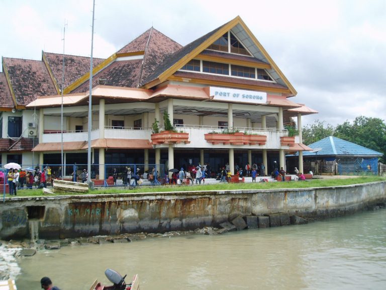 Port of Sorong passenger terminal with a red-roofed building and people waiting by the water